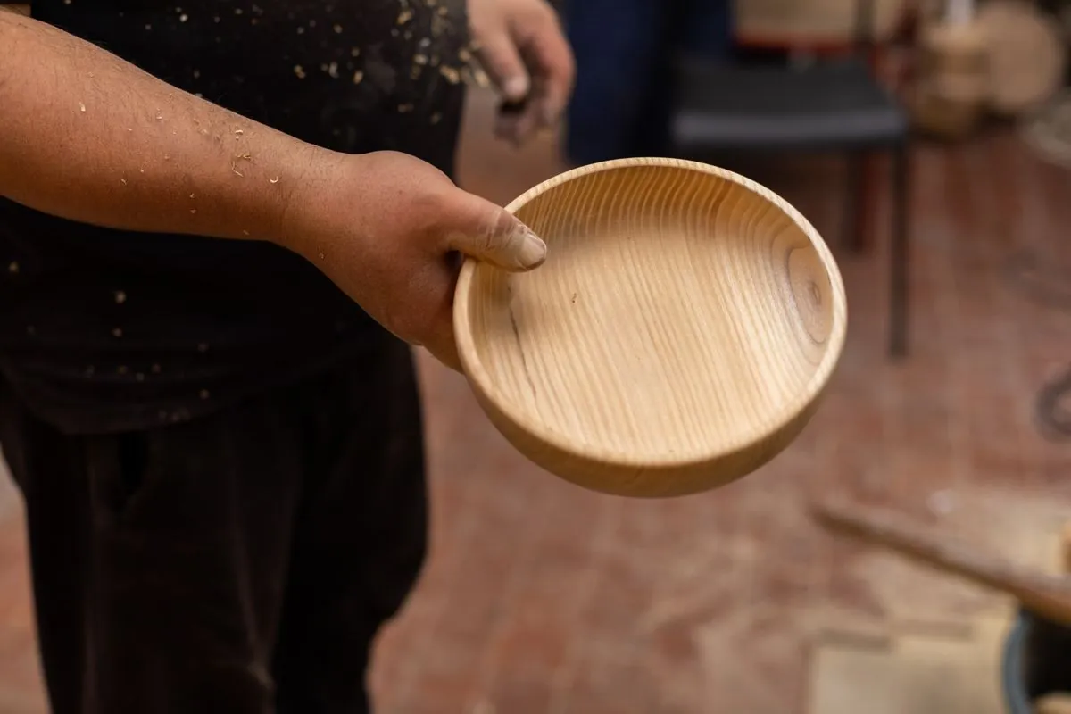 A craftsman holding a freshly turned wooden bowl in a workshop